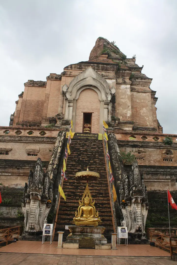 Ruiny świątyni Wat Chedi Luang z potężną ceglaną stupą, schodami prowadzącymi na szczyt i flagami buddyjskimi