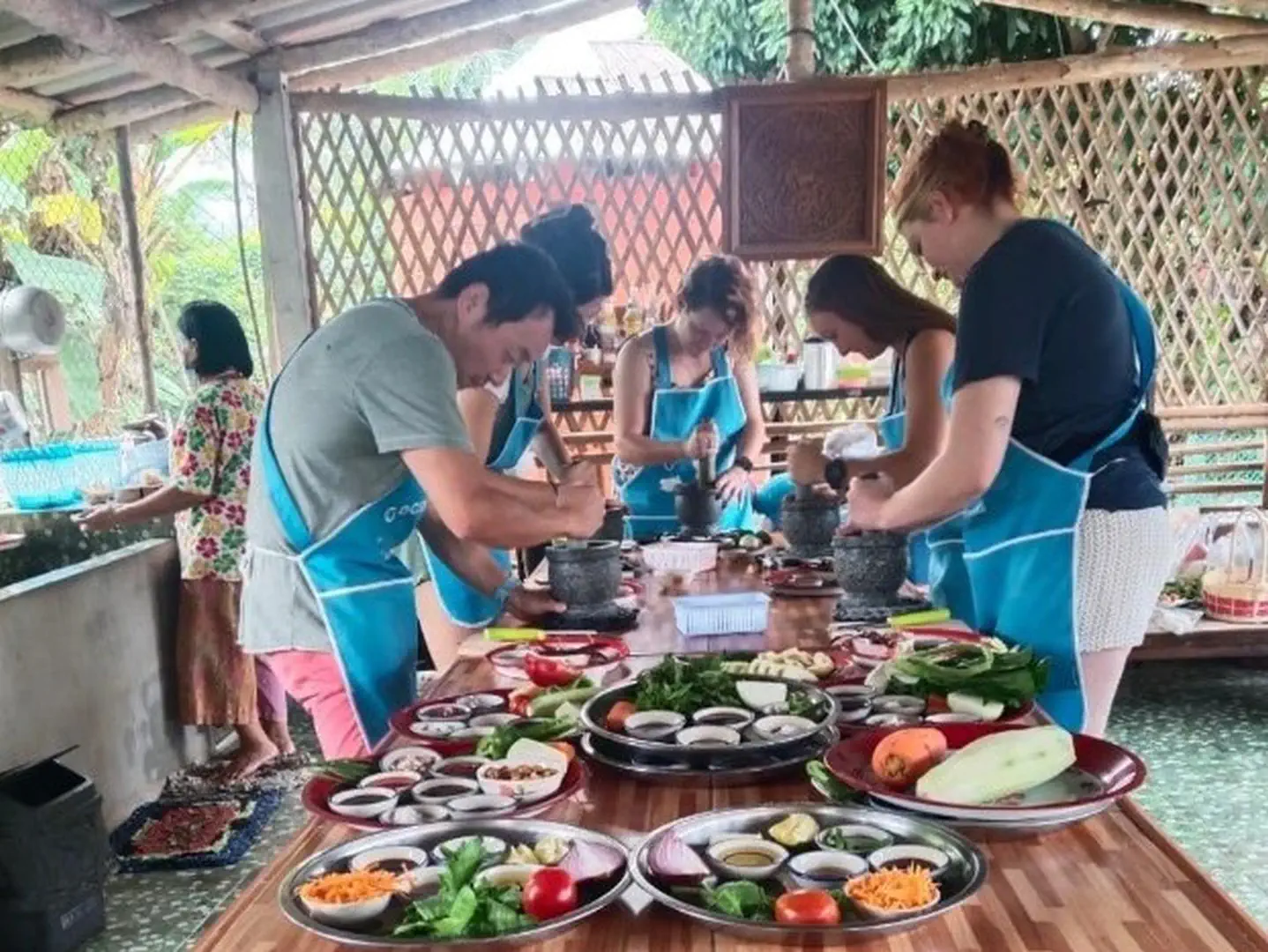 Uczestnicy kursu gotowania w Chiang Mai przygotowują dania tajskiej kuchni w otwartej, lokalnej kuchni z drewnianymi elementami.