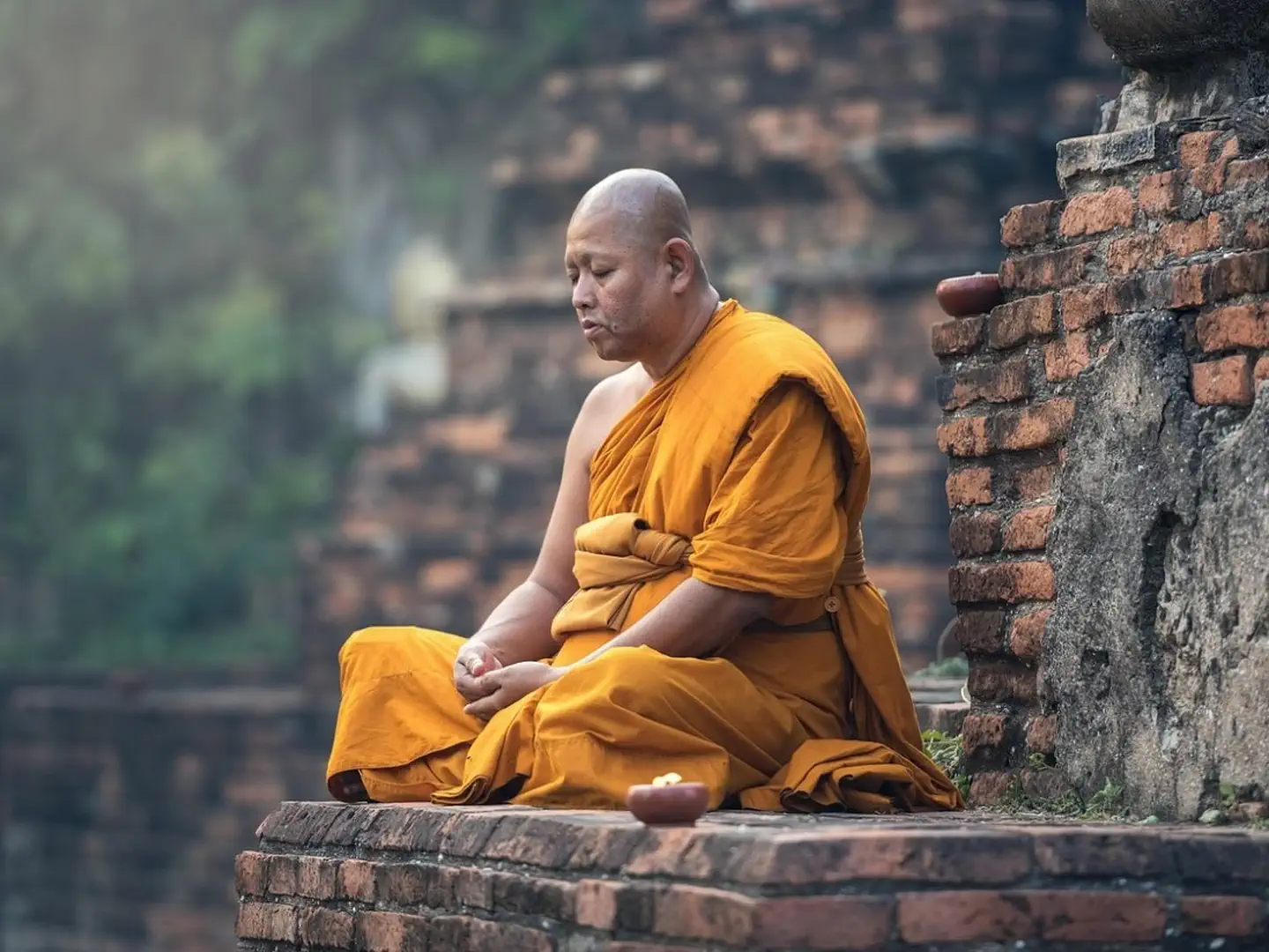Buddyjski mnich w pomarańczowych szatach medytuje na tle zabytkowych murów świątyni w Chiang Mai.