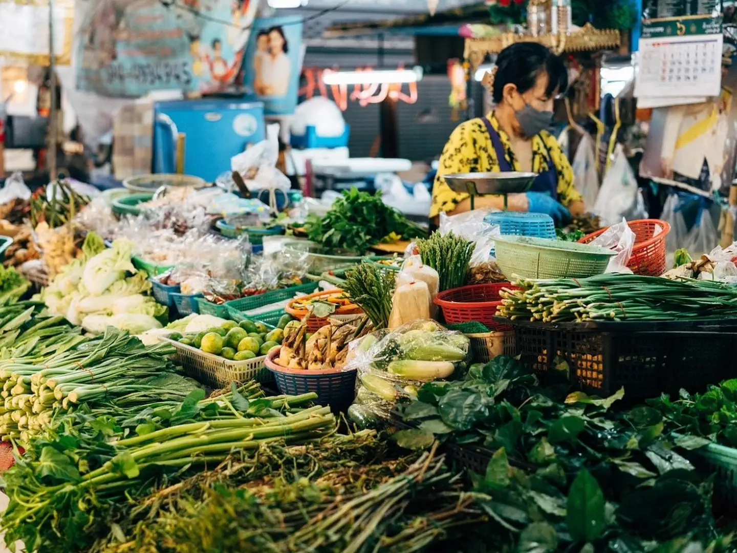 Stoisko z warzywami i ziołami na nocnym bazarze w Chiang Mai, obsługiwane przez kobietę w maseczce