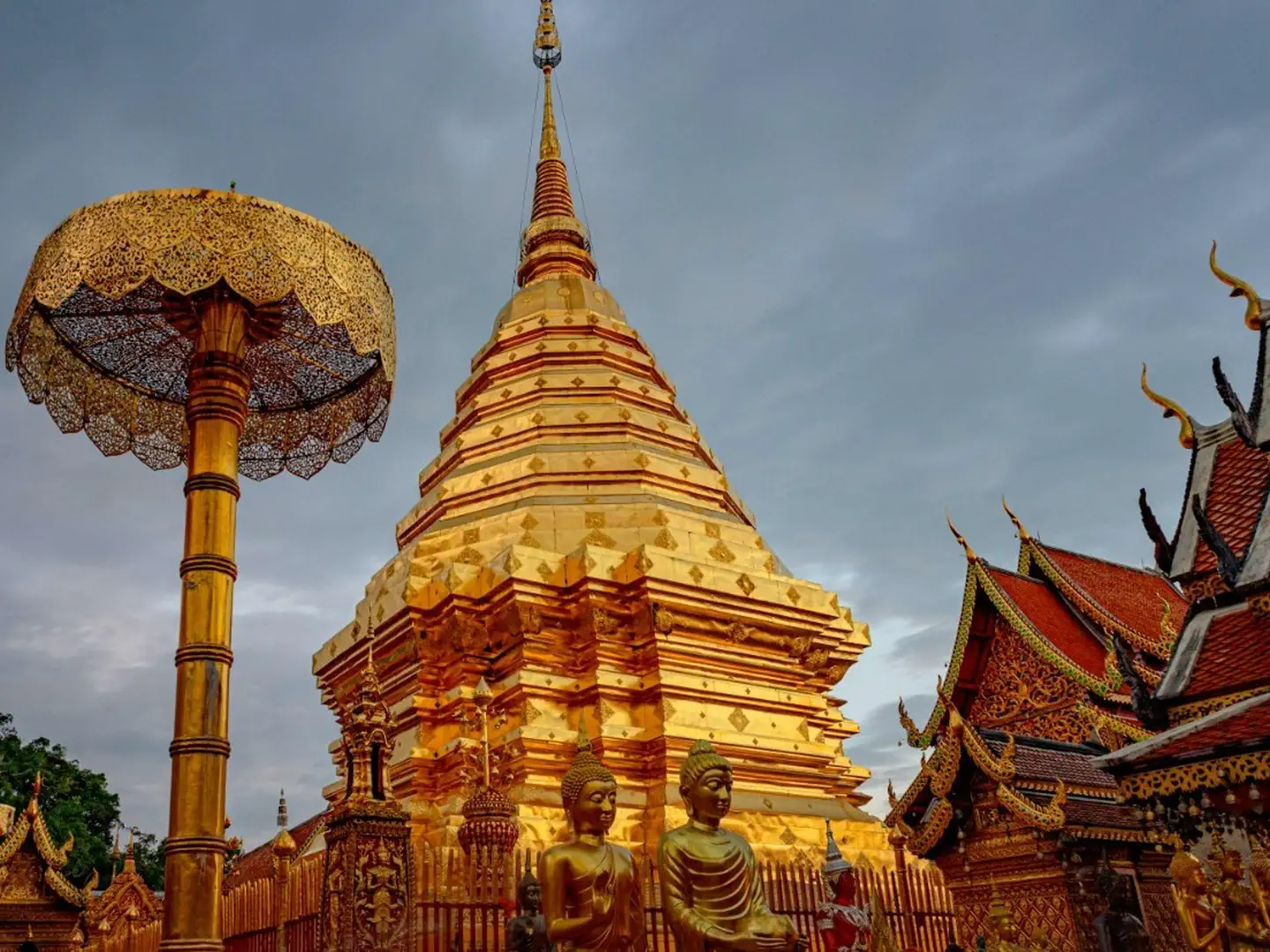 Złota stupa świątyni Wat Phra That Doi Suthep otoczona posągami Buddy, parasolami ceremonialnymi i zdobionymi dachami świątyni